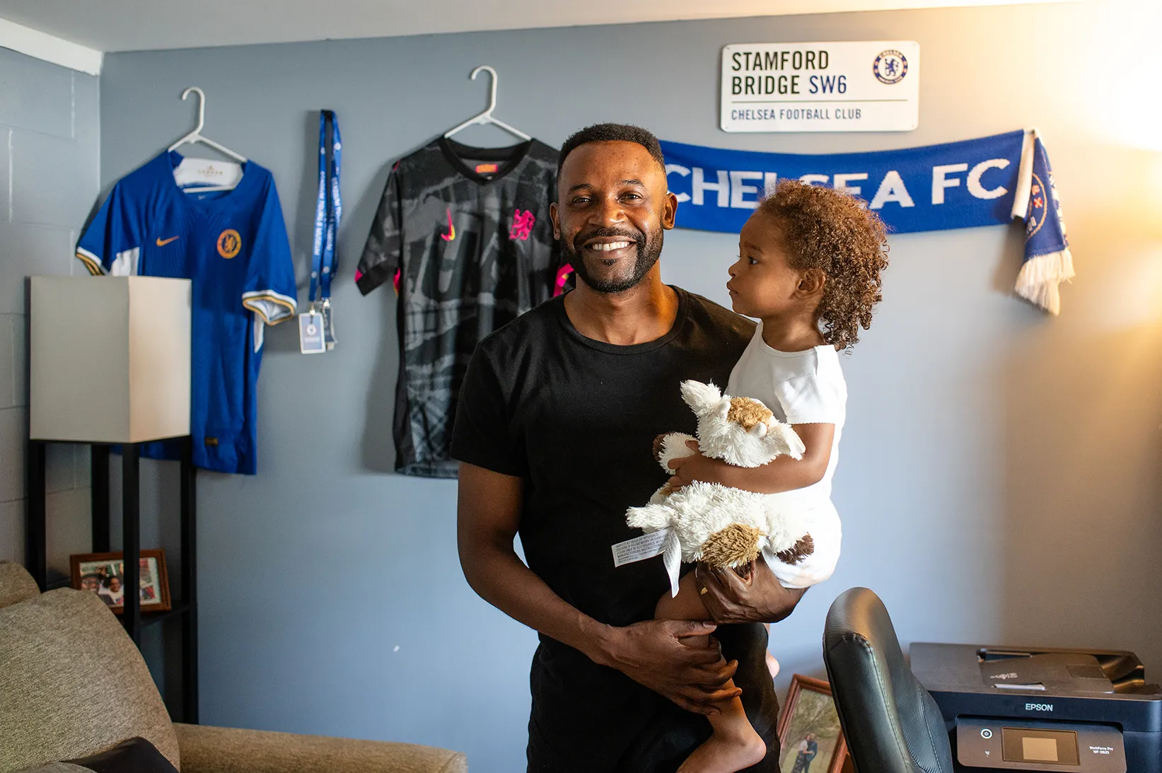 Jon and his daughter posing in front of Chelsea Football Club memorabilia